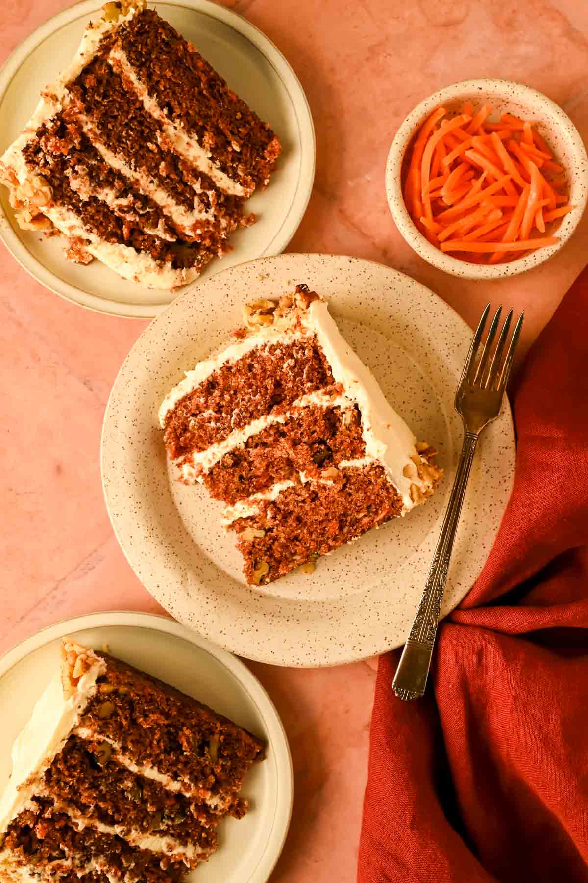 3 slices of cream cheese frosted carrot cake on a white and gold plate.