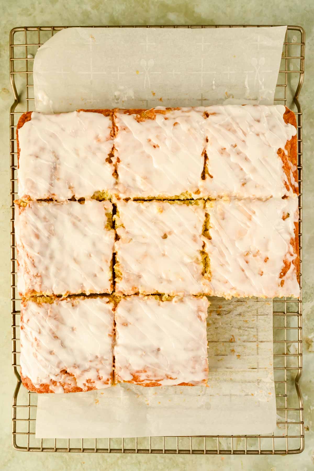 glazed lemon zucchini cake sliced into squares on wire cooling rack.