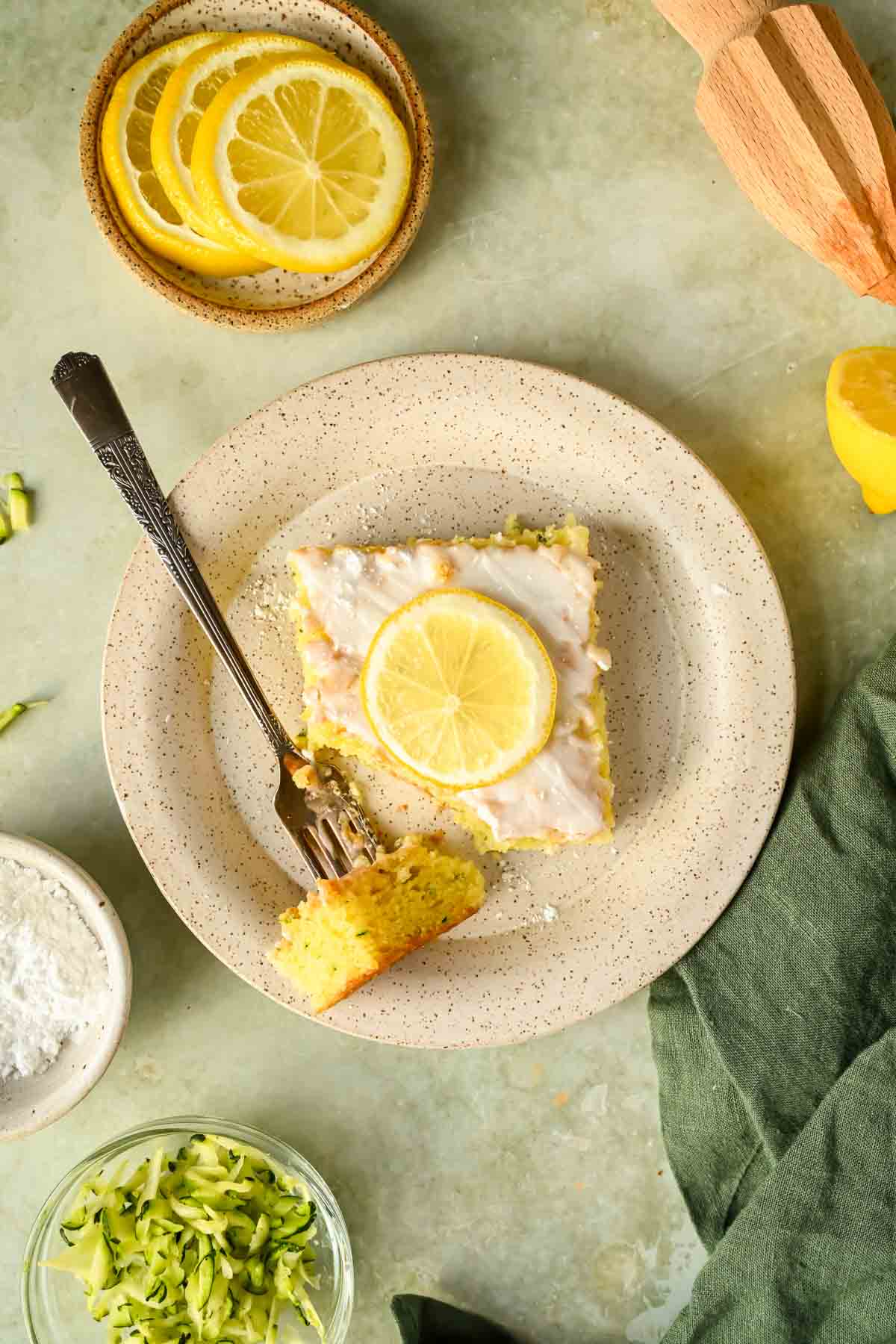 slice of lemon zucchini cake glazed with lemon slice on top on speckled plate.
