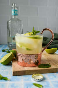 a copper mug filled with tequila mule, lime wedges, and mint sprigs.