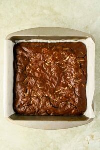 baked brownies in square baking dish lined with parchment paper.