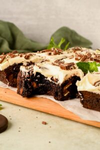frosted andes mint brownies sliced into squares with chopped andes mints and mint leaves on top.