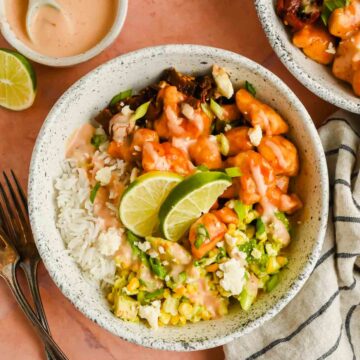 bed of rice topped with honey chipotle chicken and avocado salad garnished with lime wedges.