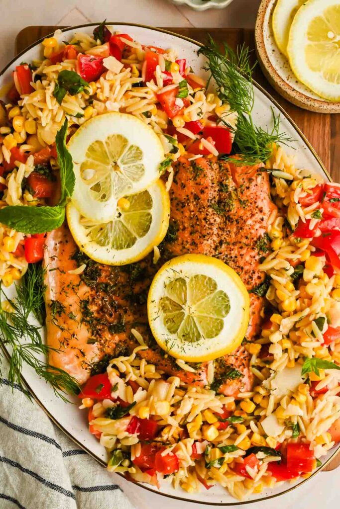 orzo salad topped with flaky steelhead trout and lemon wedges.