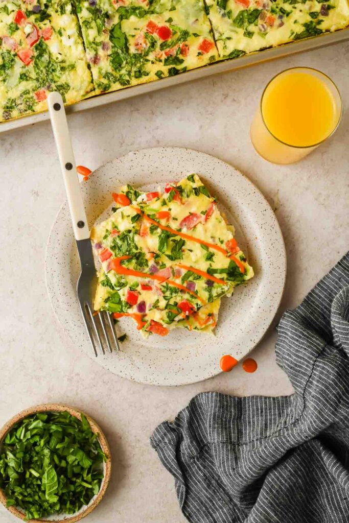 two slices of baked sheet pan omelette with spinach and bell peppers stacked on each other on small plate.