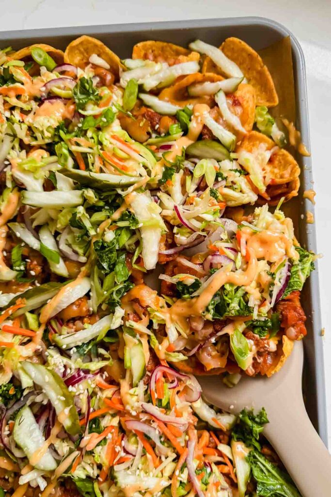 loaded sloppy joe nachos topped with cheese, slaw, green onion and spicy mayo on sheet pan.