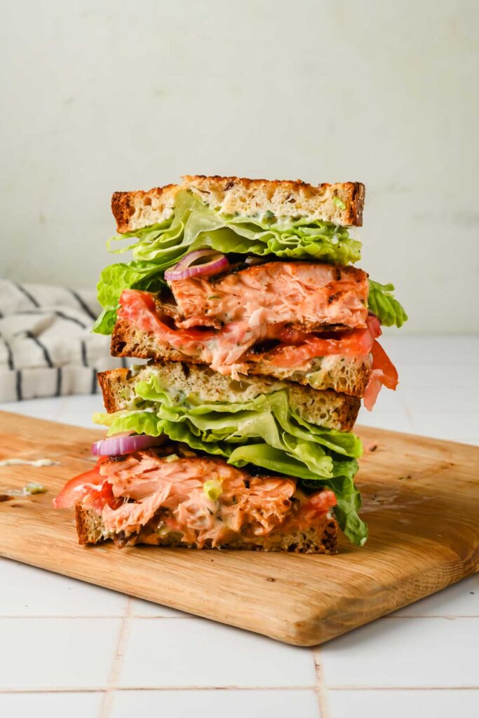 two stacked halves of a salmon BLT on a wood cutting board.
