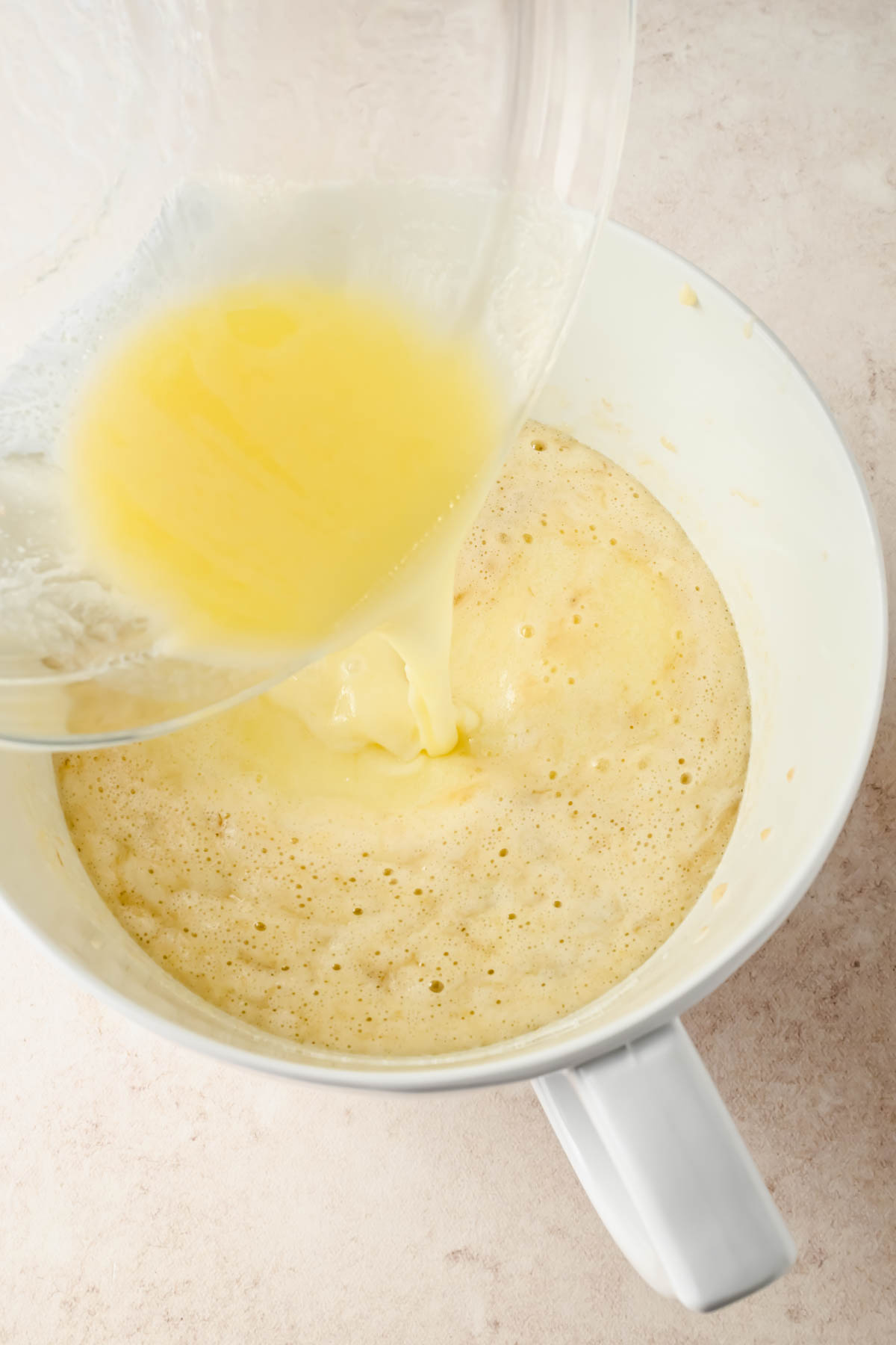 pouring melted butter into bowl of wet ingredients for banana sheet cake.
