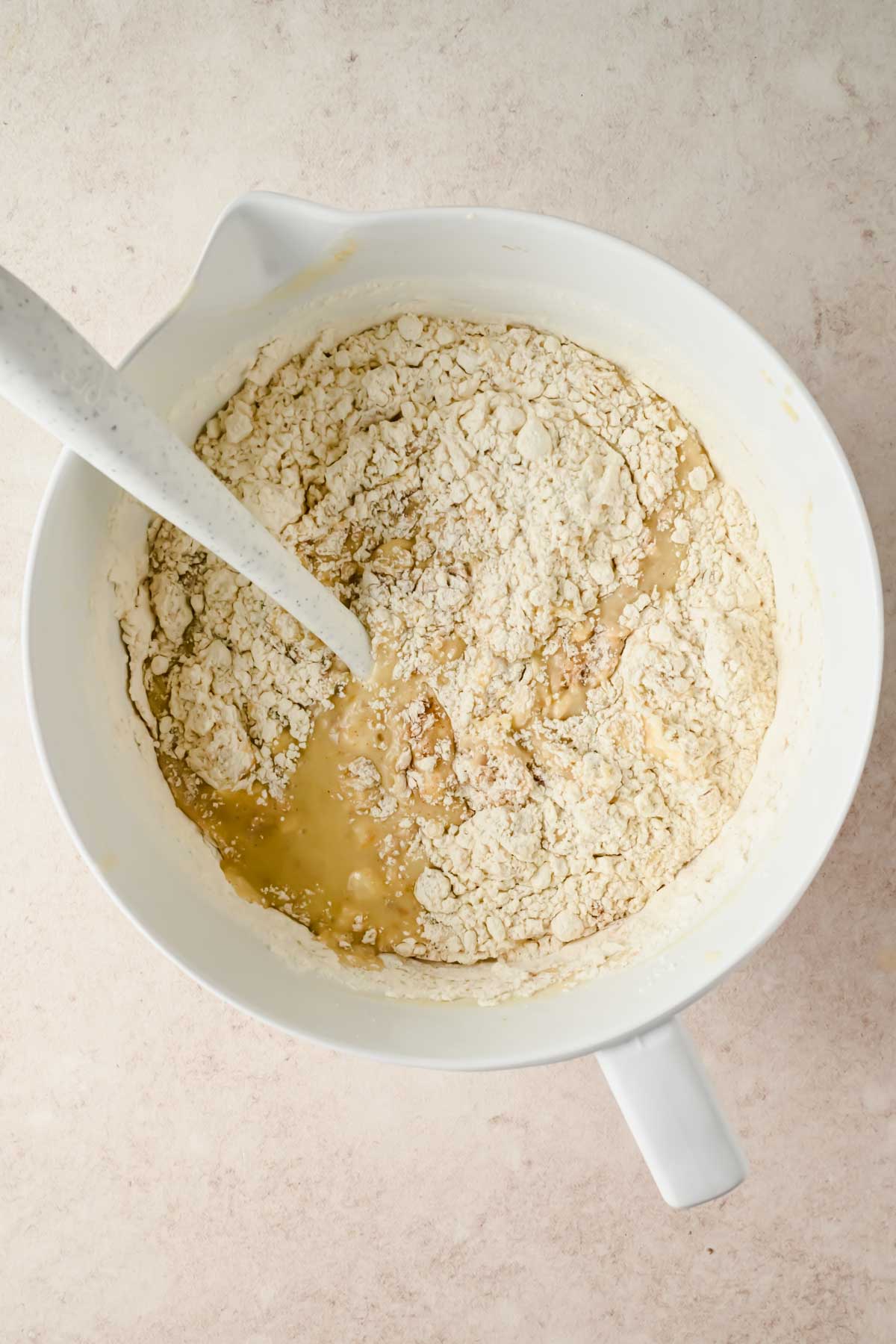 mixing flour into bowl of wet ingredients of banana sheet cake batter.