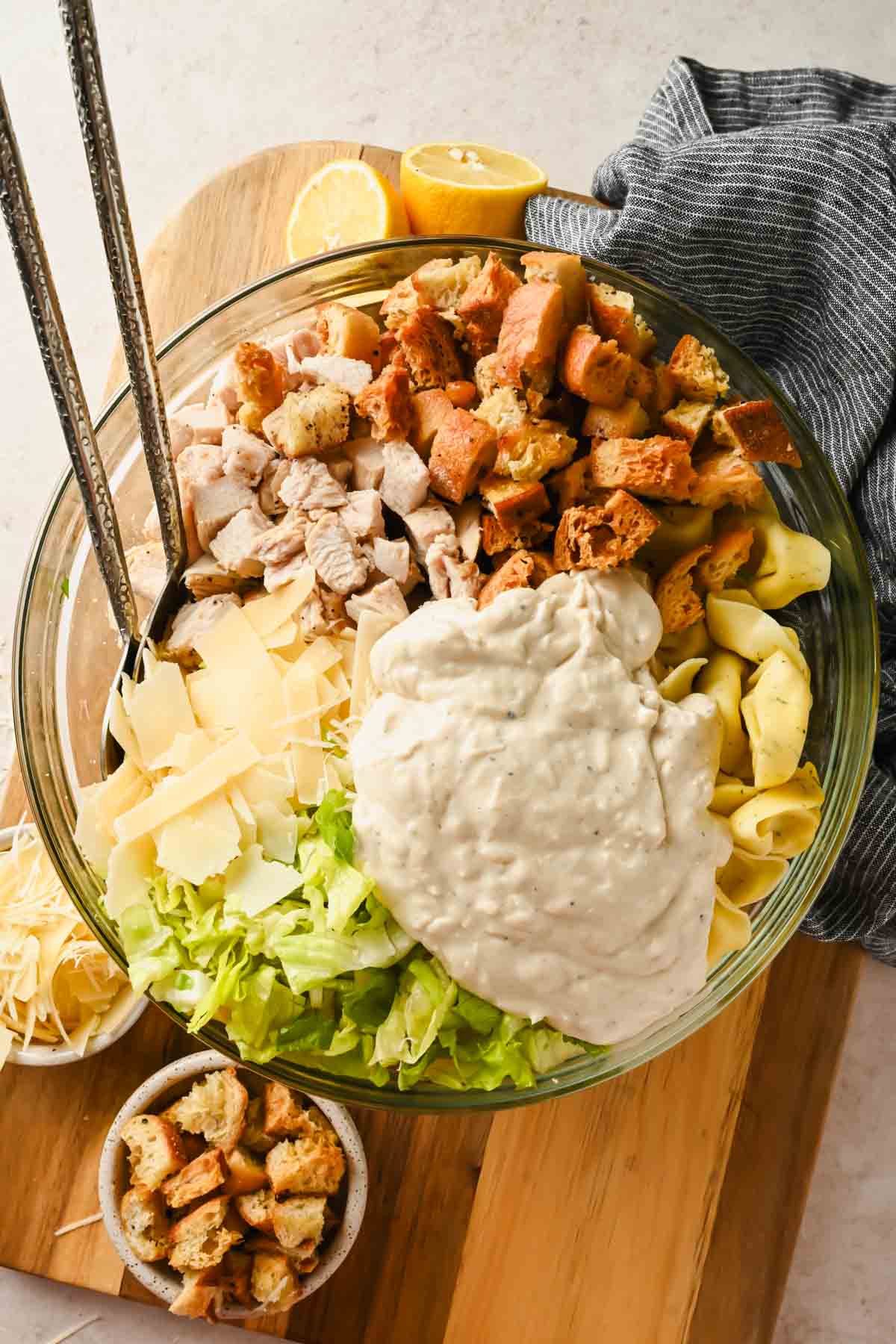 tortellini pasta salad with caesar dressing ingredients with tongs prior to tossing in glass bowl.