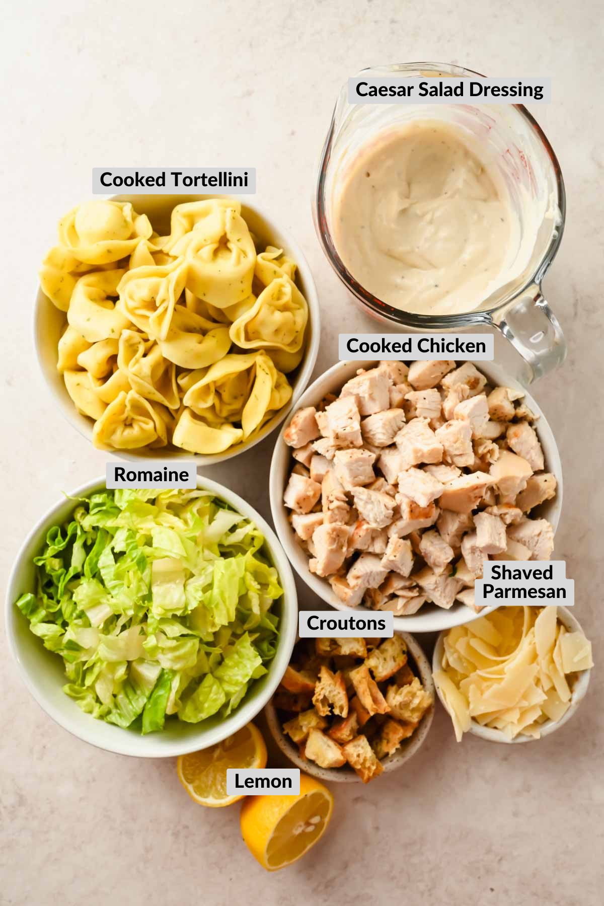 labeled ingredients for tortellini pasta salad with caesar dressing in individual bowls.