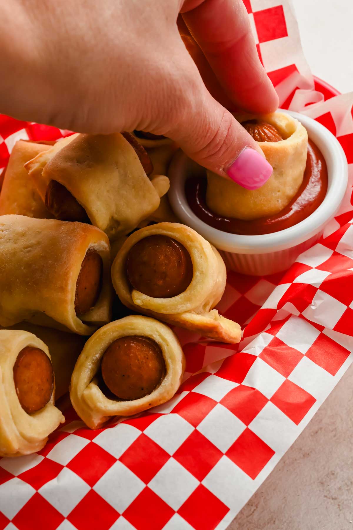 hand dunking pigs in a blanket into small bowl of ketchup.