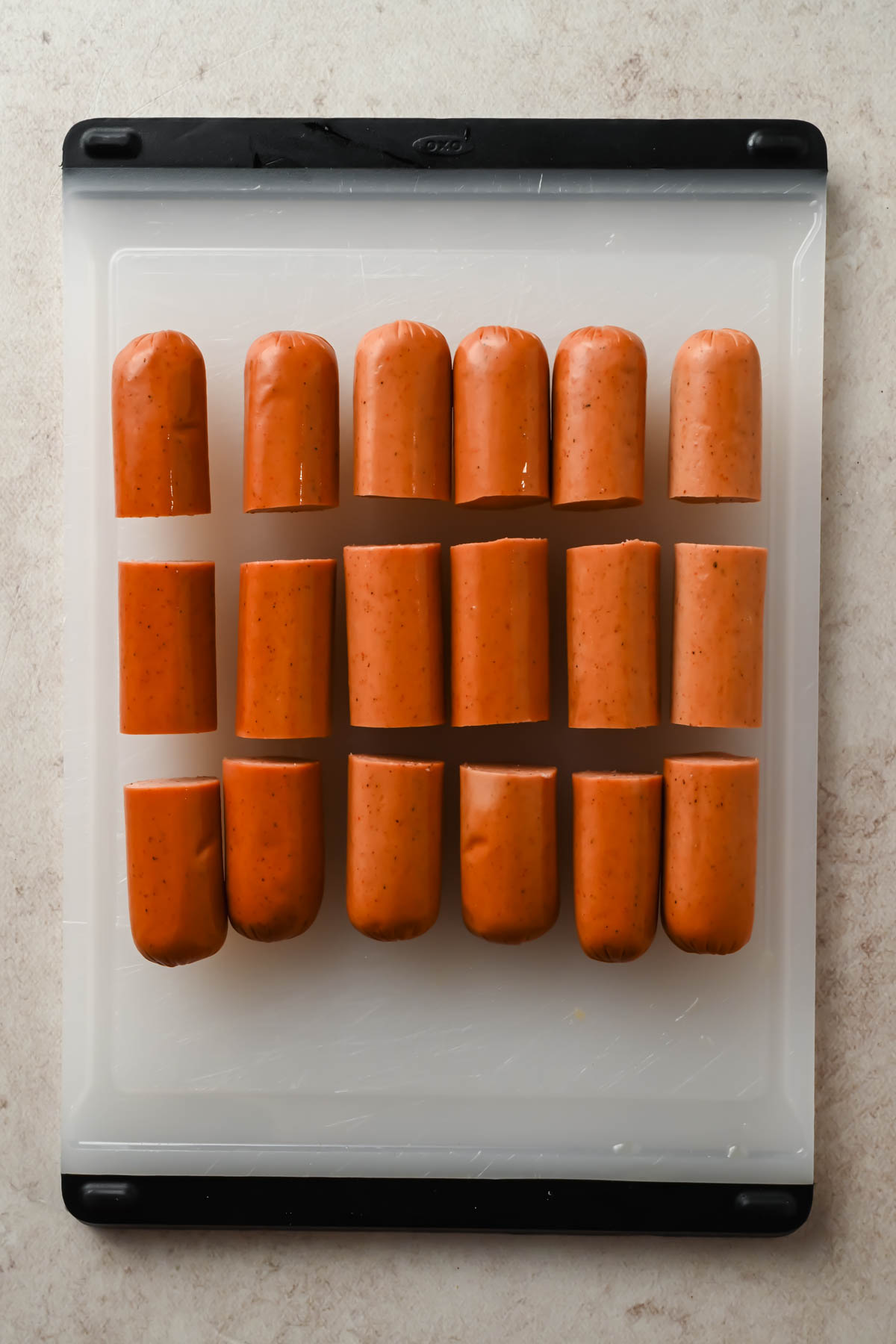 six hot dogs each cut into thirds on white cutting board.