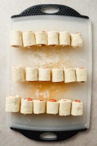 18 mini pigs in a blanket rolled up on white cutting board before cooking.