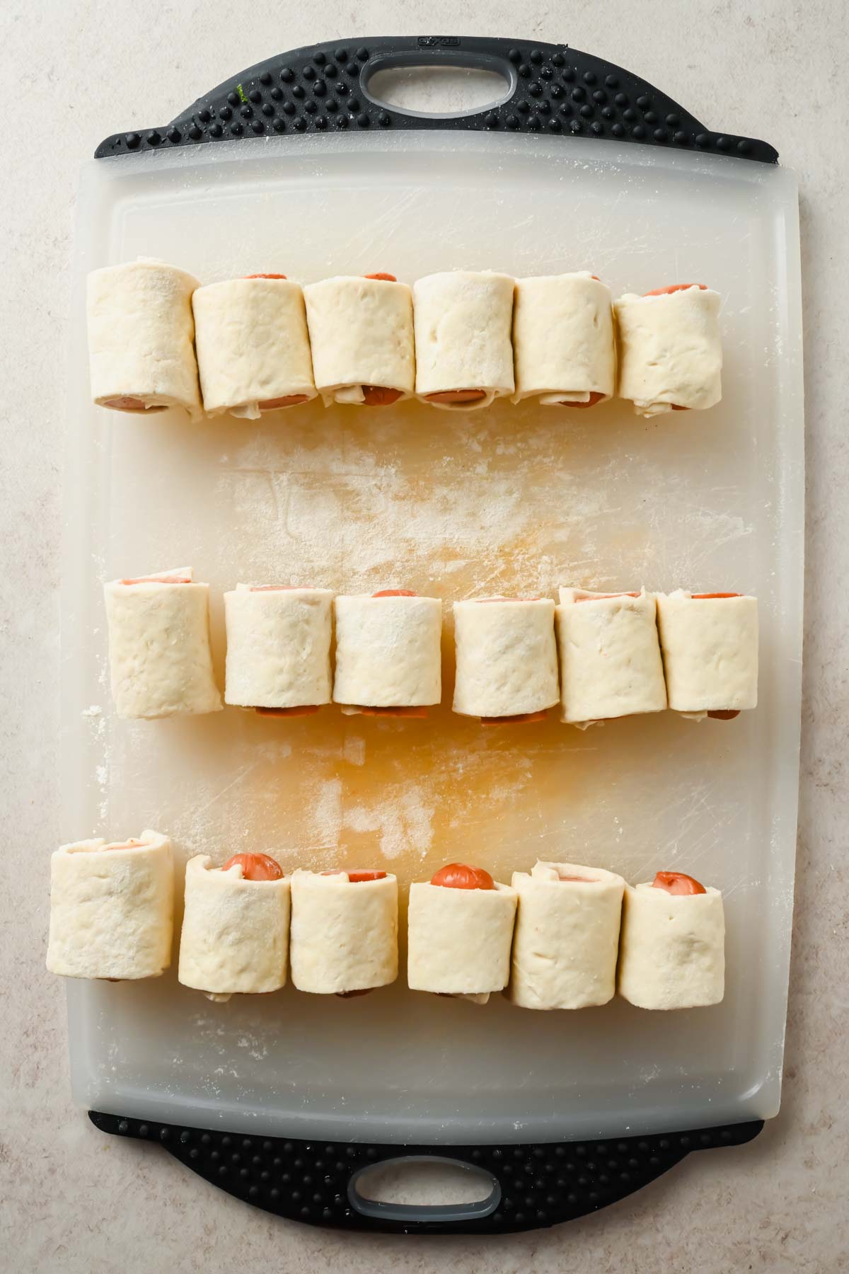 18 mini pigs in a blanket rolled up on white cutting board before cooking.