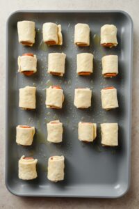 18 mini pigs in a blanket rolled up on gray sheet pan before cooking.