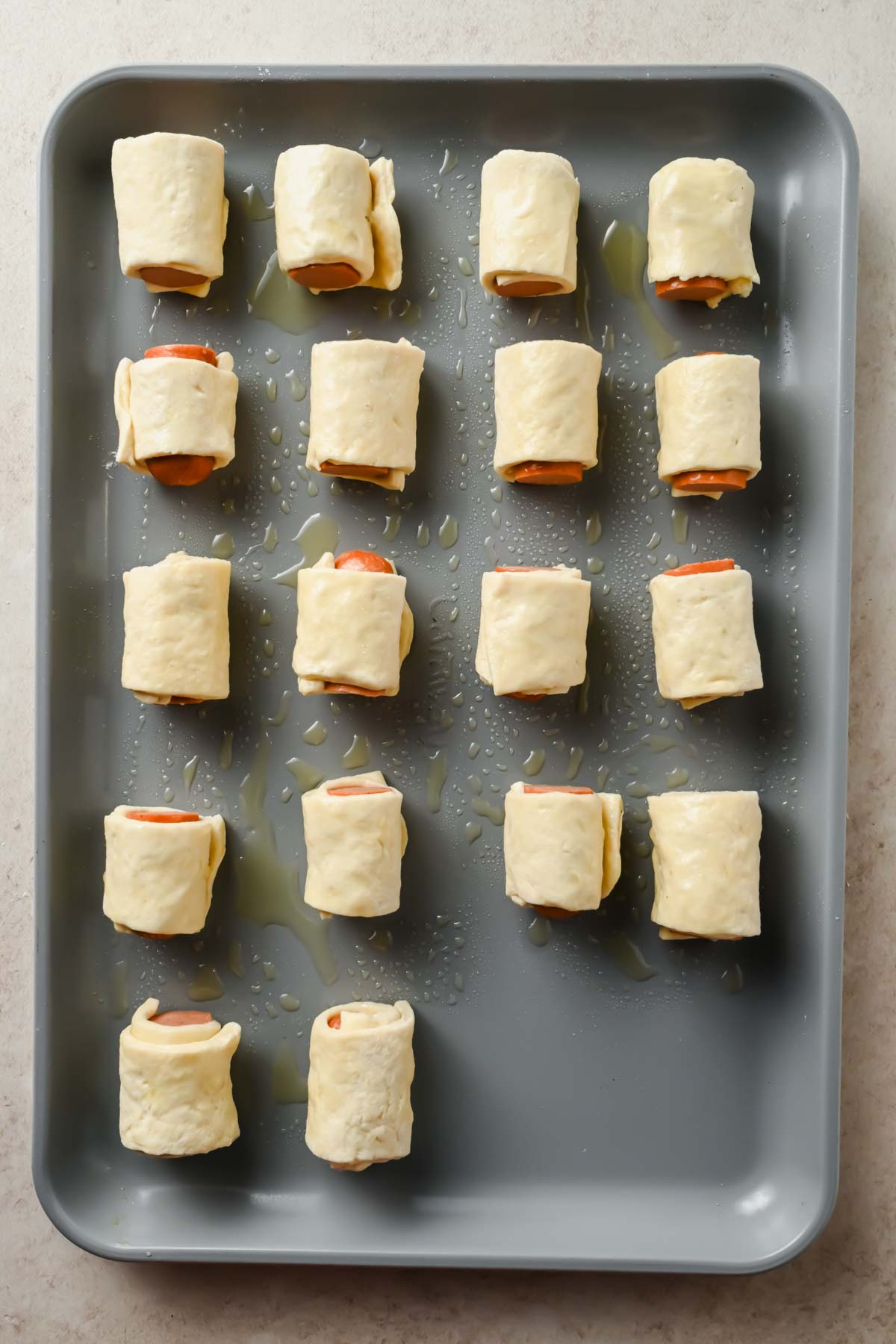 18 mini pigs in a blanket rolled up on gray sheet pan before cooking.