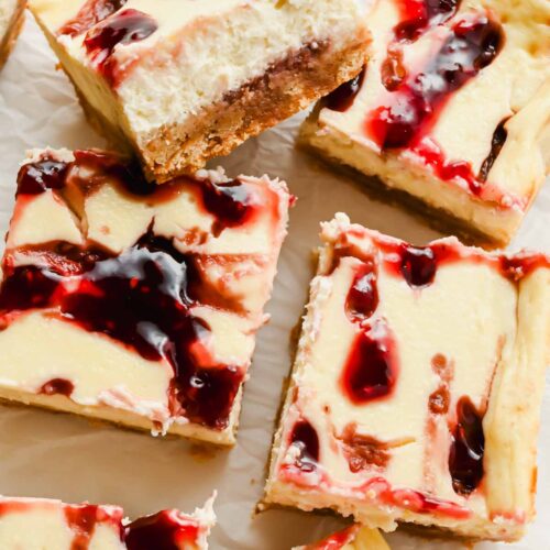 Squares of protein cheesecake bars with raspberry swirl on parchment.