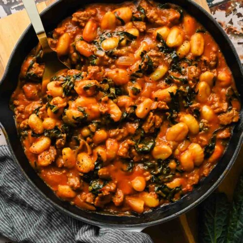 large cast iron skillet with pumpkin gnocchi and saut&eacute;ed kale with large serving spoon in skillet.