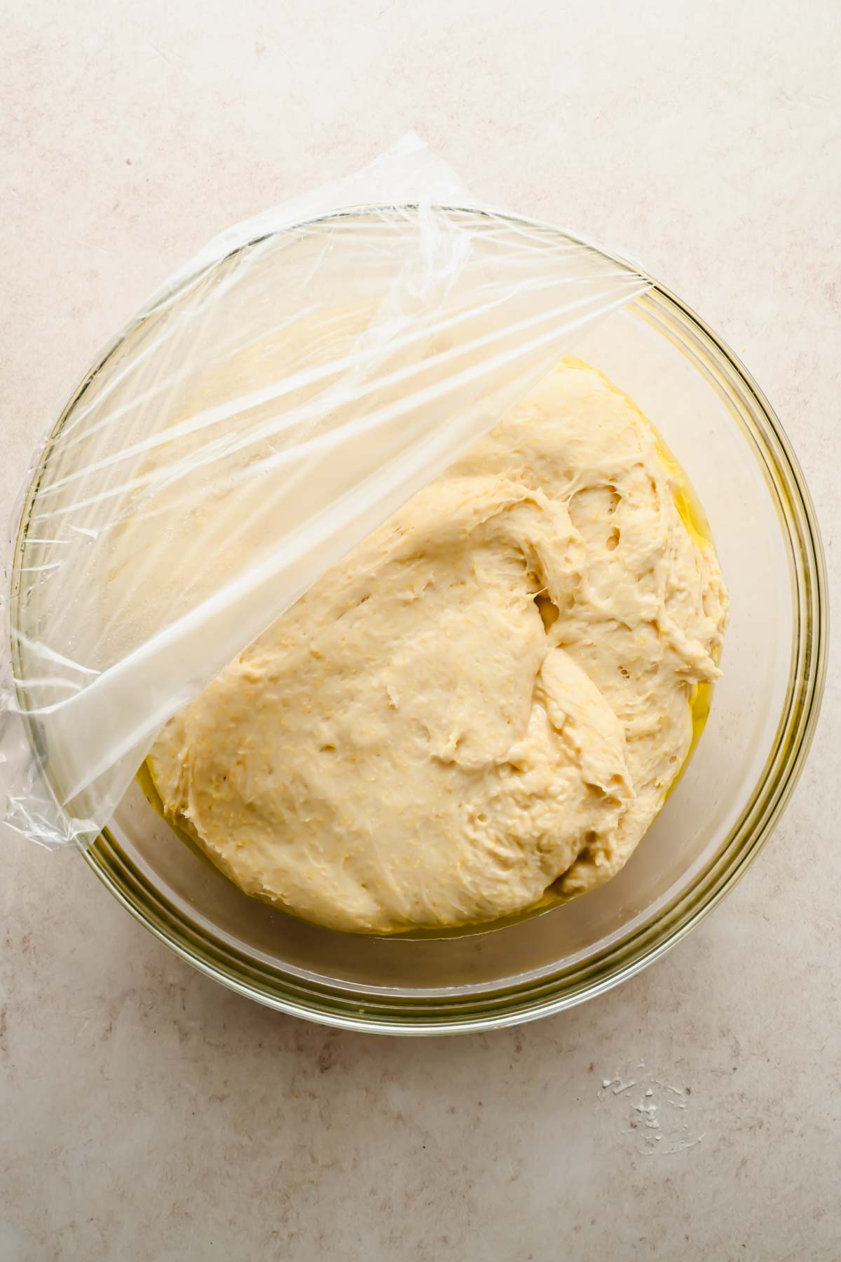 raw focaccia cornbread dough prior to it rising in glass mixing bowl covered with plastic wrap.