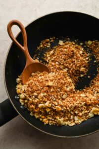 toasted bread crumbs in black skillet with wooden spoon in pan.