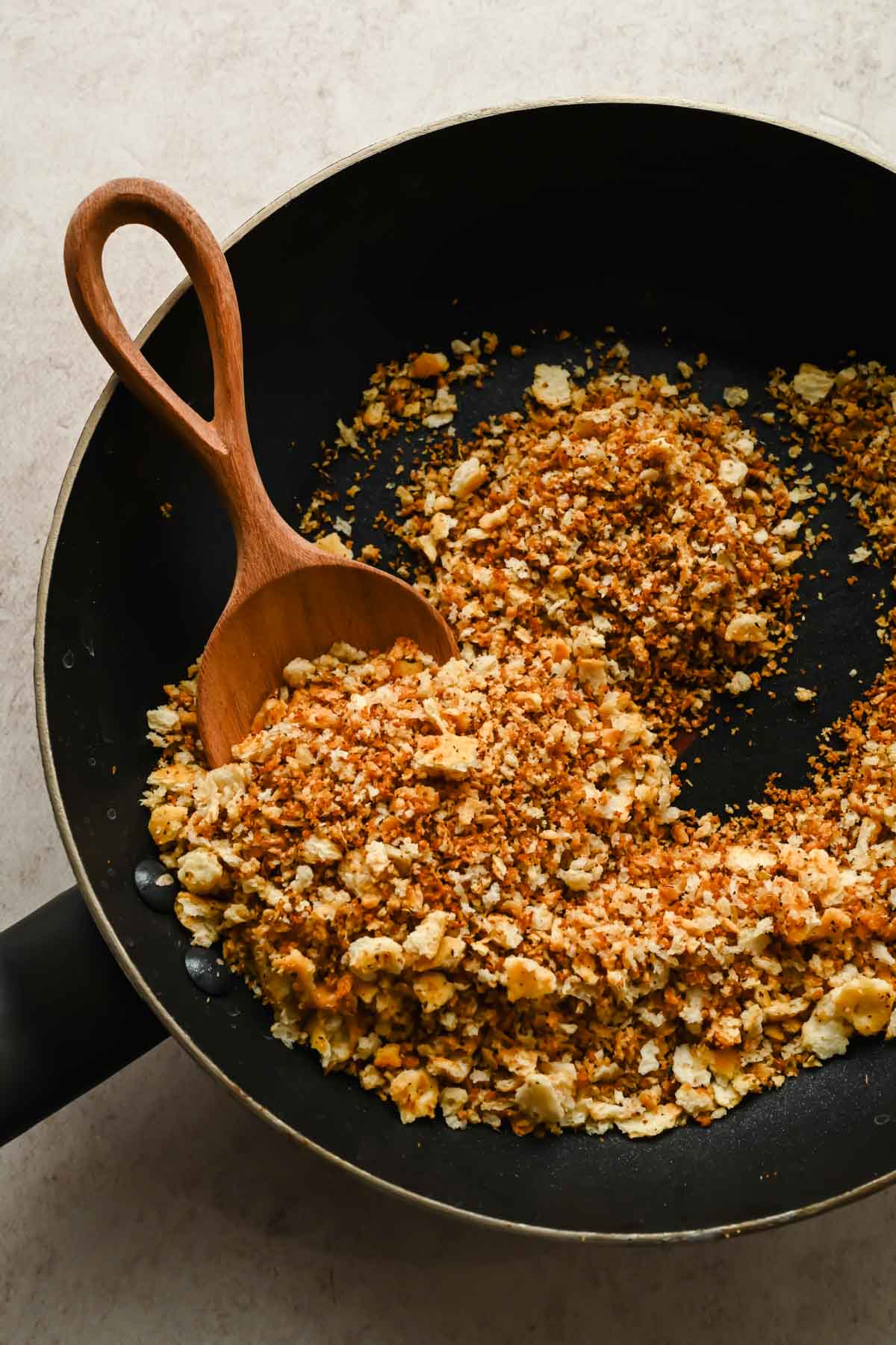 toasted bread crumbs in black skillet with wooden spoon in pan.