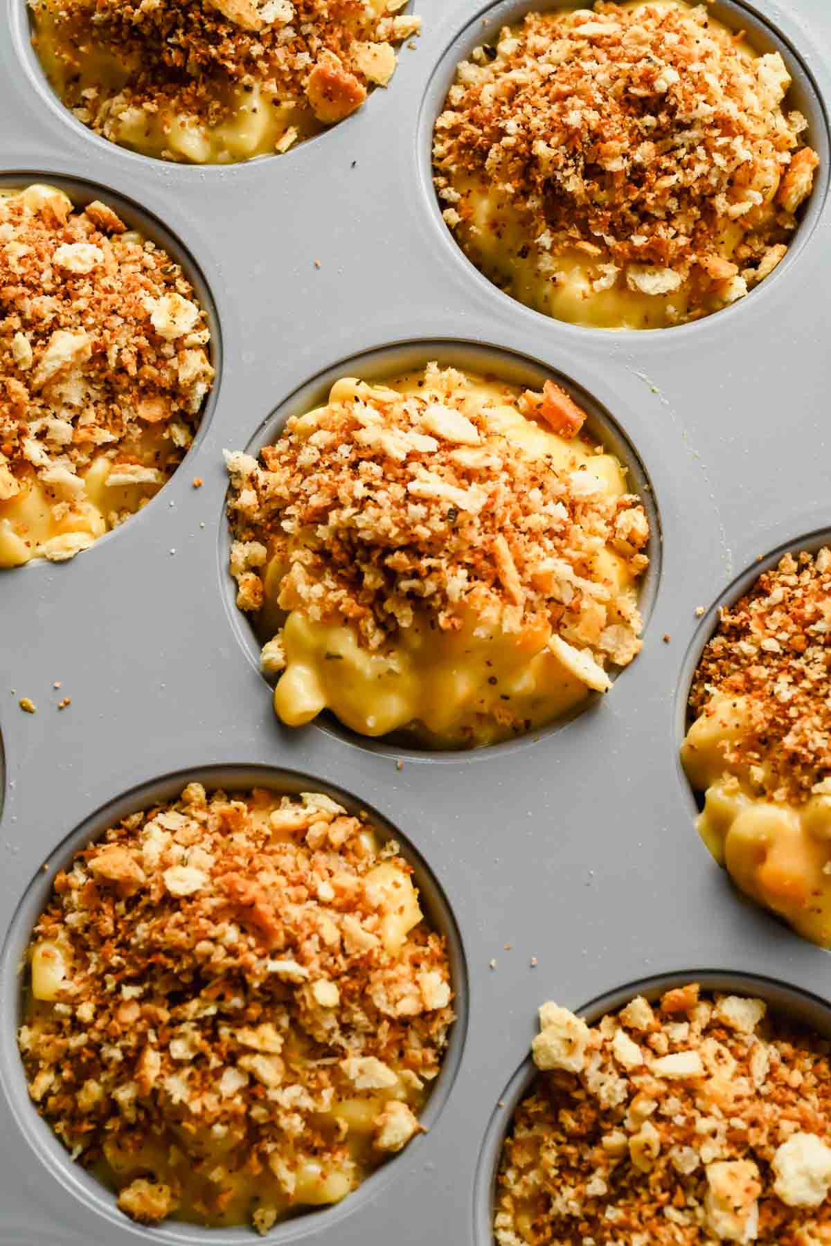 mac and cheese muffins in gray muffin tin topped with bread crumbs.