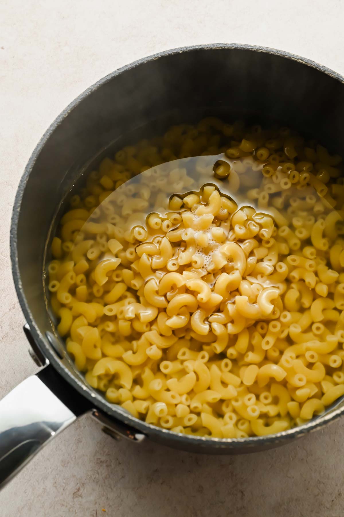 elbow noodles in water cooking in black sauce pot.