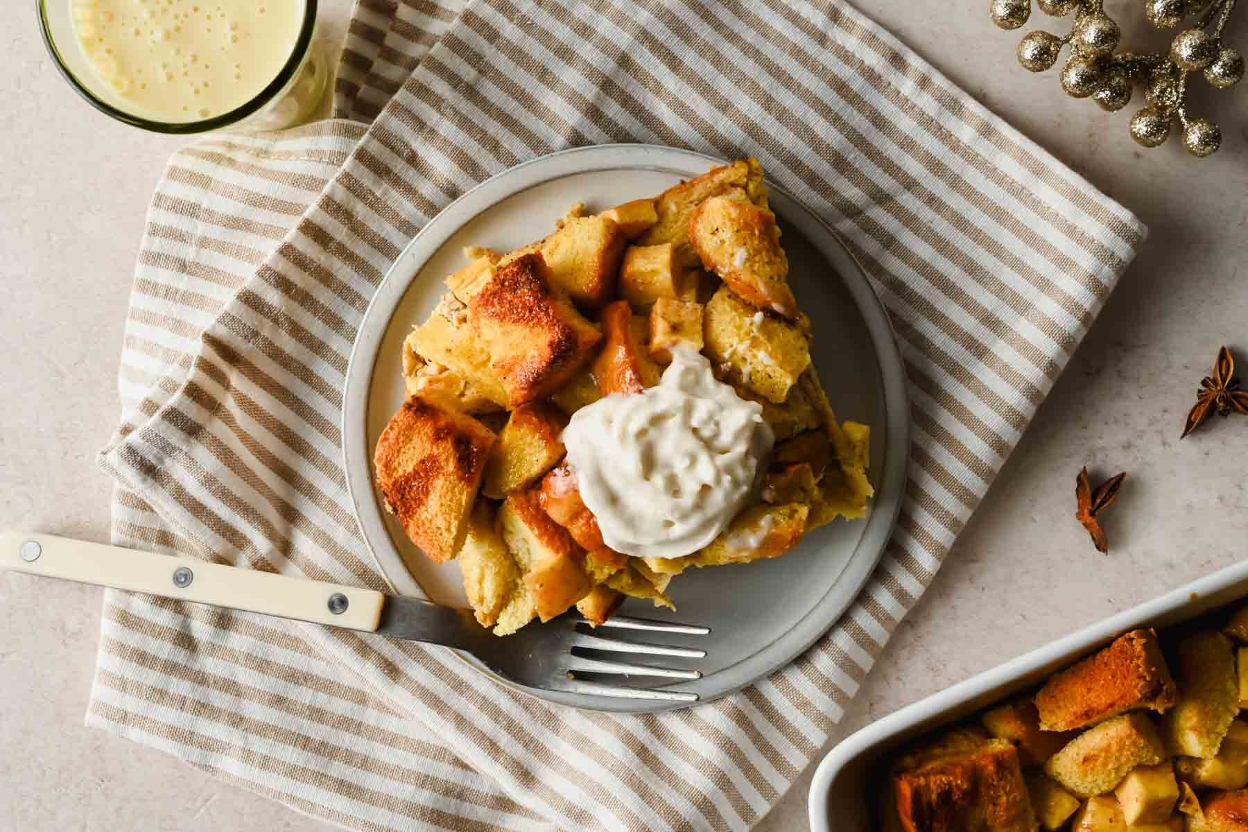 slice of eggnog french toast casserole topped with whipped cream on serving plate with fork.