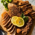 sliced turkey tenderloins on wood cutting board topped with herbs and lemon slices.