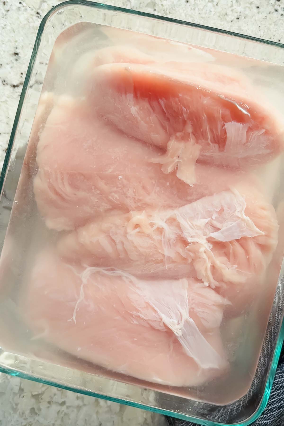 4 turkey tenderloins lined up in glass baking dish drowned in salt water brine.