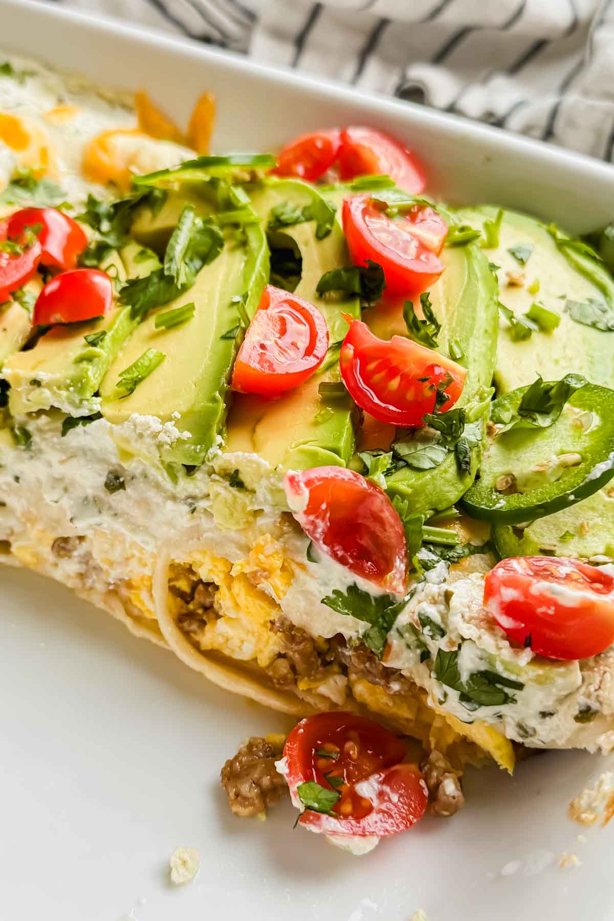 close up of breakfast enchiladas topped with sliced tomato, avocado, cheese and creamy green sauce.