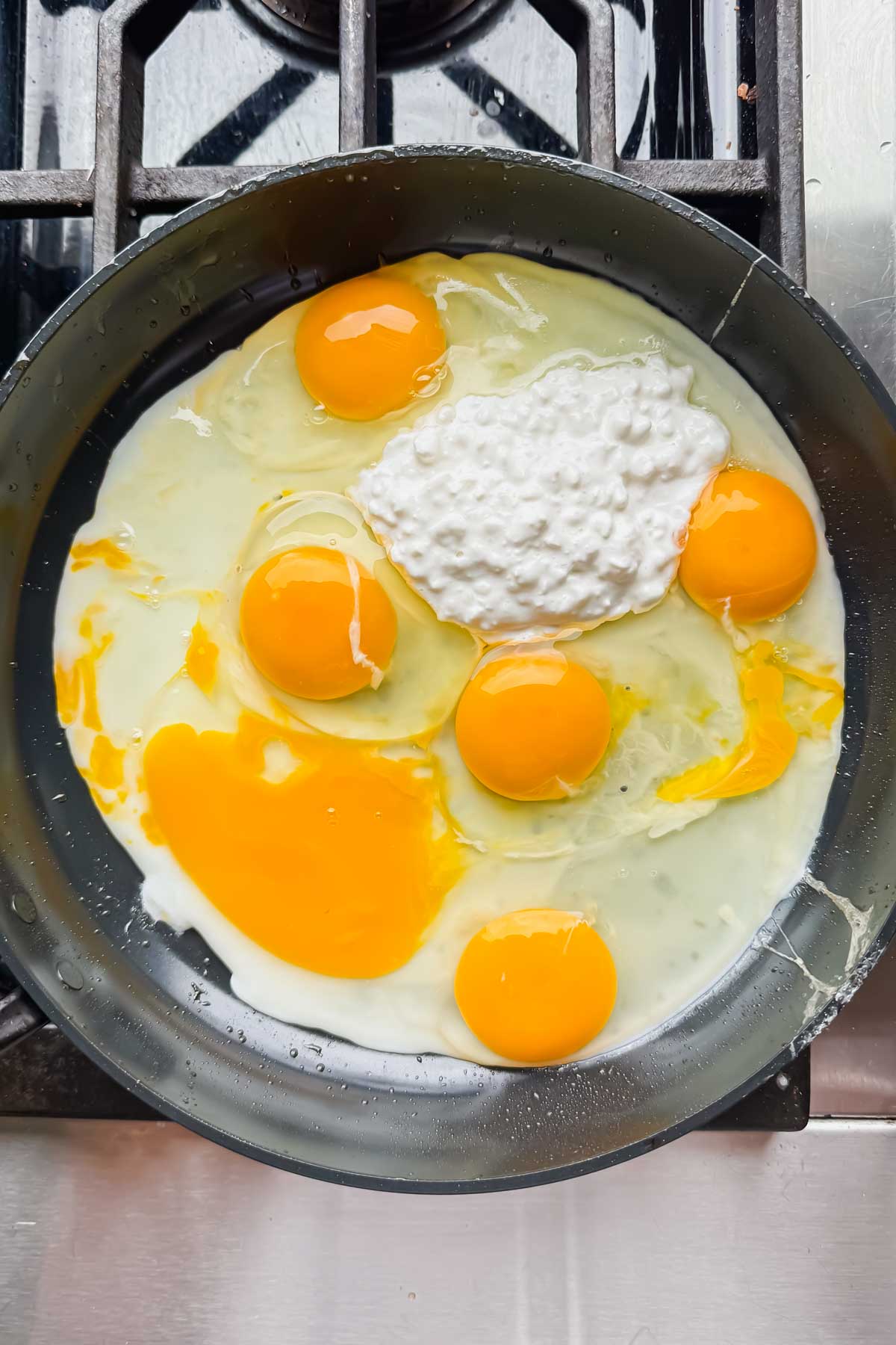 raw eggs and cottage cheese in black skillet on burner.