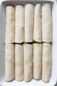 10 rolled tortillas aligned in two rows in white baking dish.