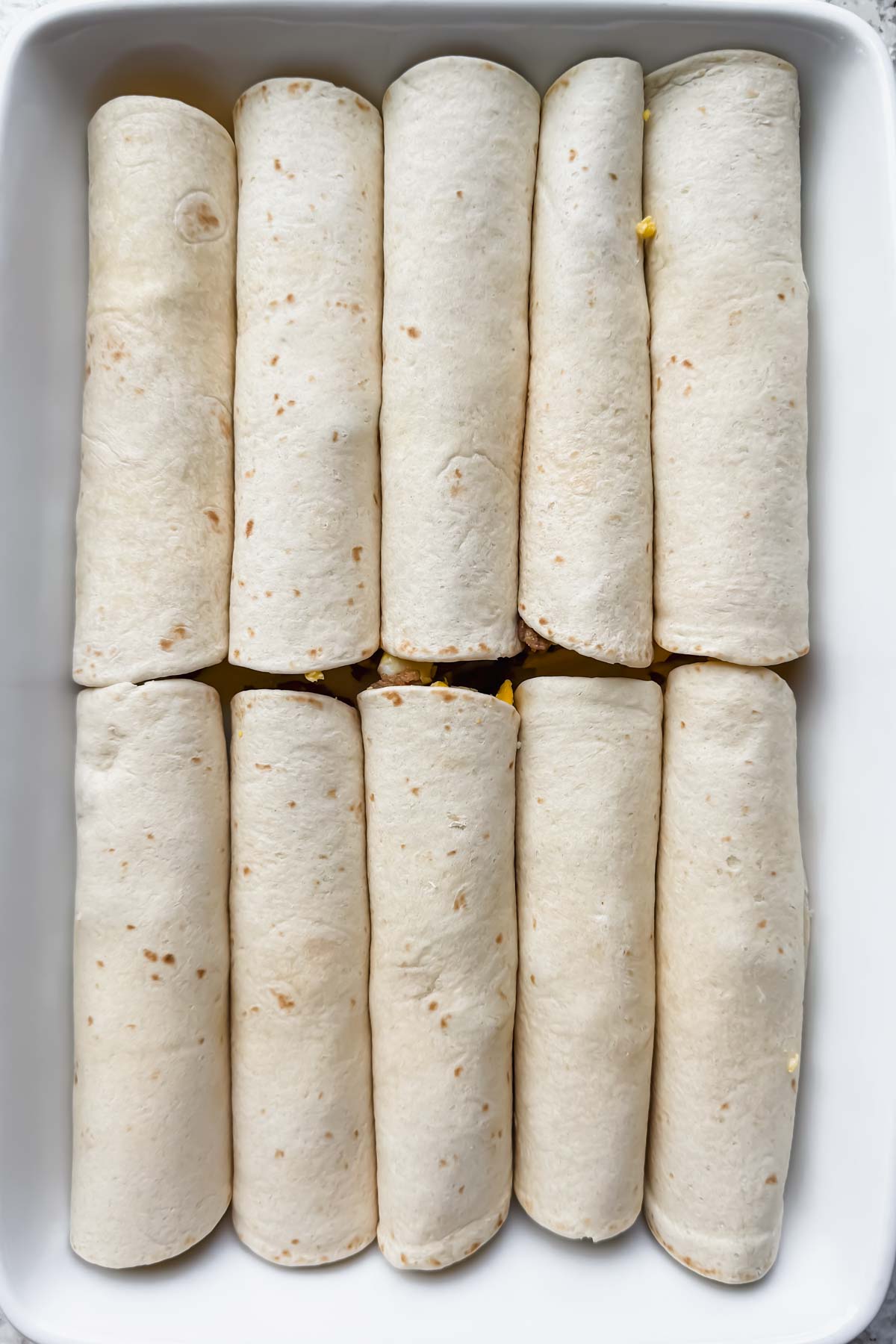 10 rolled tortillas aligned in two rows in white baking dish.