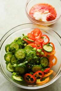 cucumber and mini bell peppers sliced thin in large glass bowl.