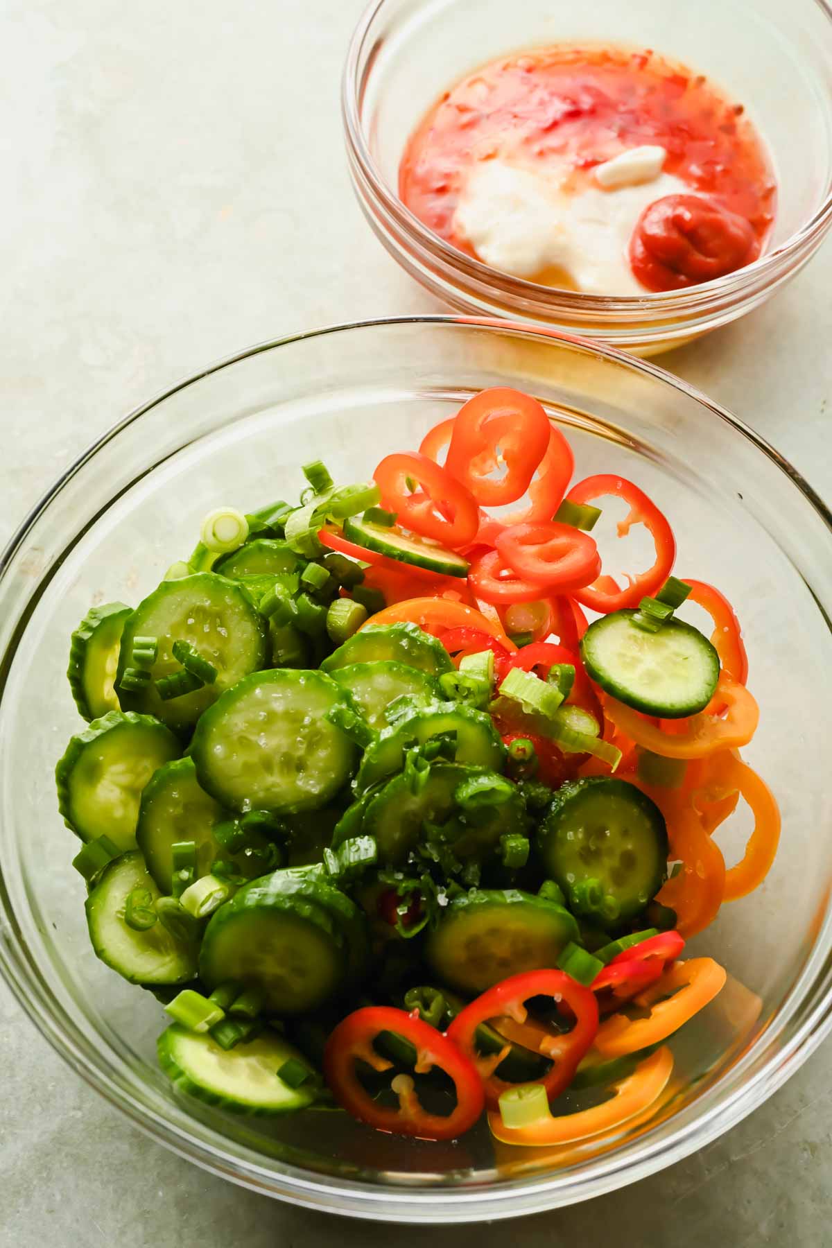 cucumber and mini bell peppers sliced thin in large glass bowl.