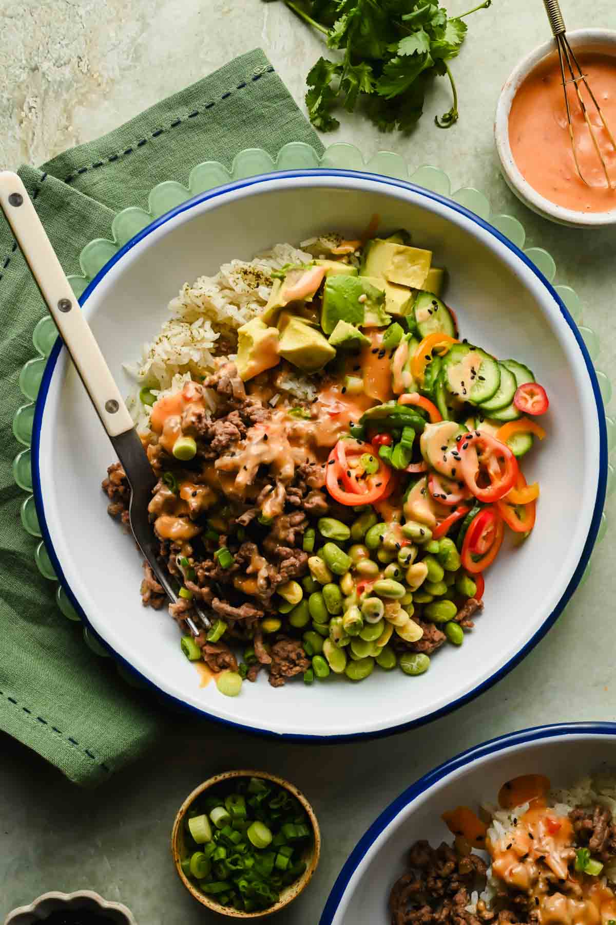 ground beef bang bang bowl with sliced avocado, edamame and bell peppers drizzled in sauce.
