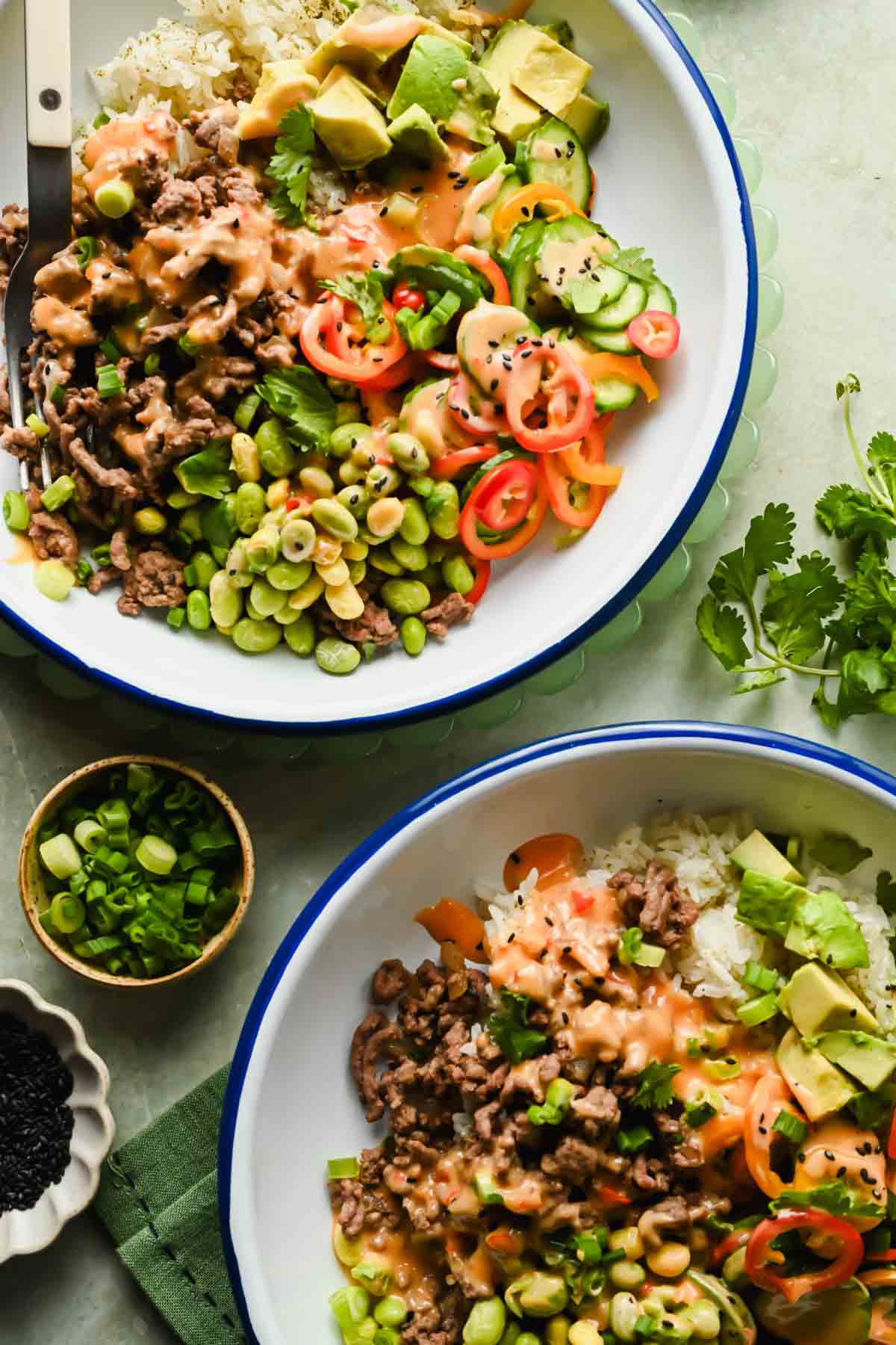 ground beef bang bang bowl with sliced avocado, edamame and bell peppers drizzled in sauce.