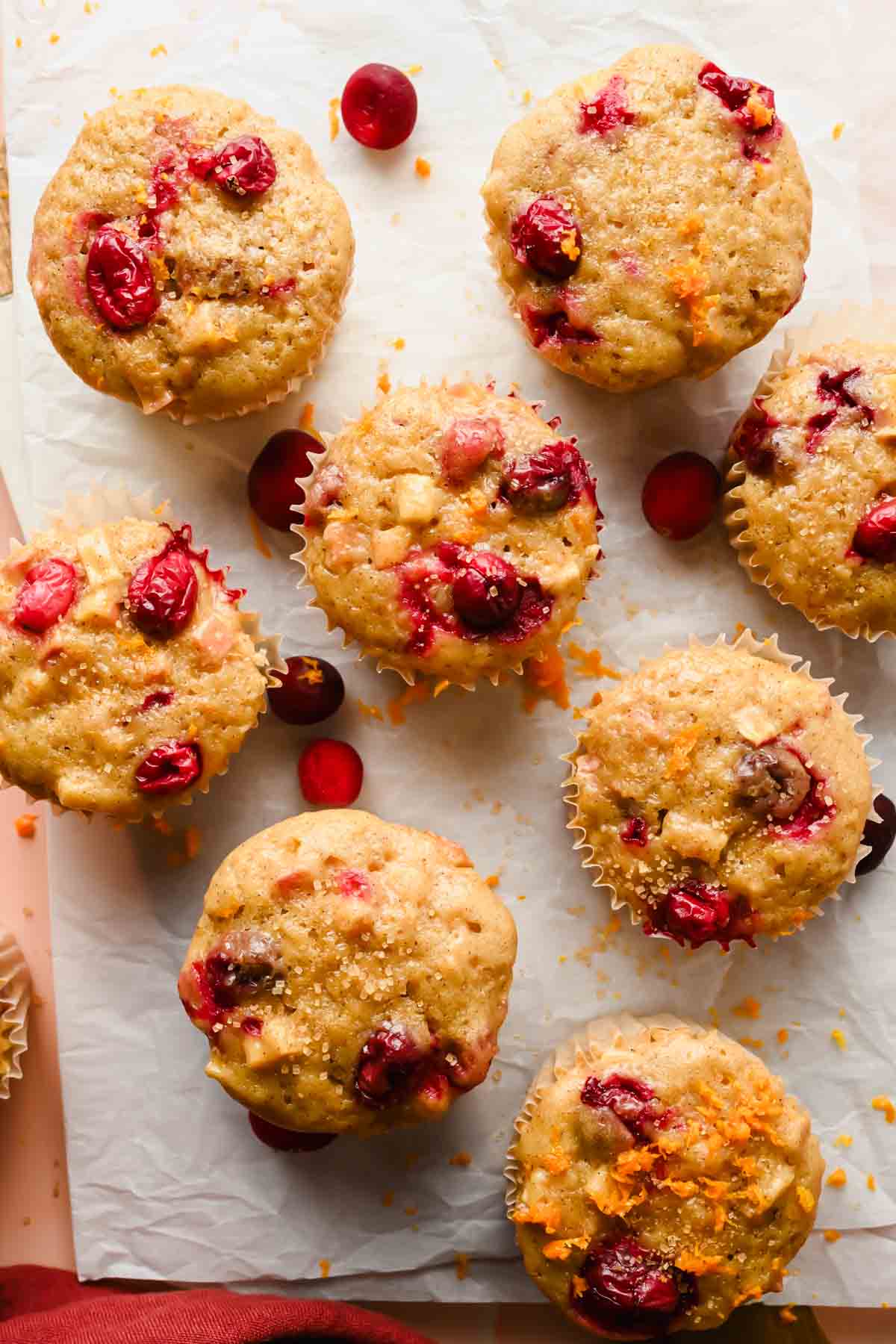 8 cranberry apple muffins on parchment paper with extra cranberries and orange zest sprinkled on top.
