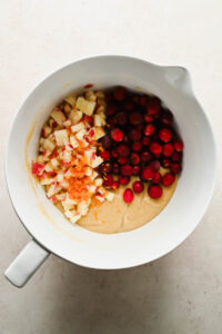 cranberries and diced apples added to muffin batter in large white mixing bowl.