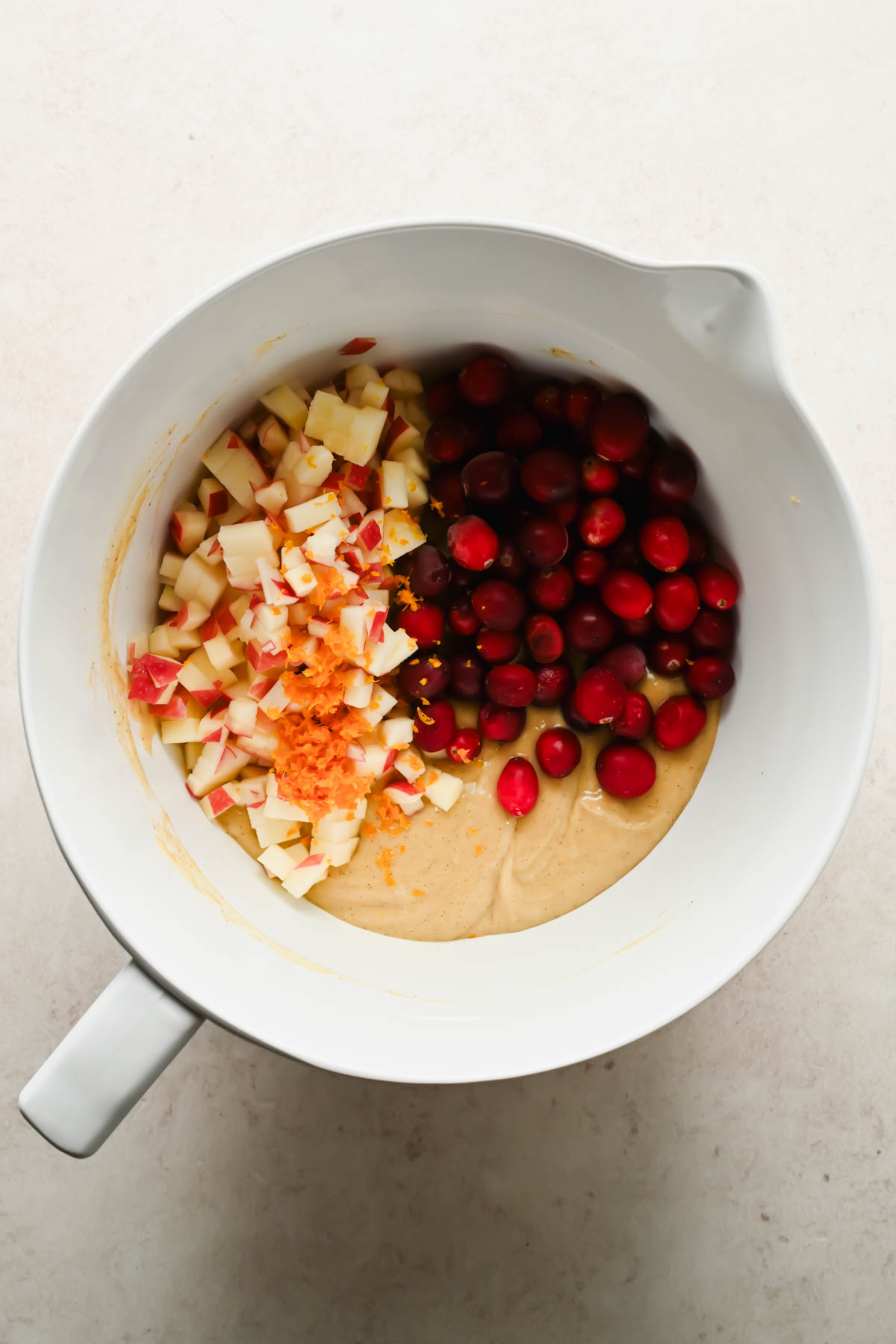 cranberries and diced apples added to muffin batter in large white mixing bowl.
