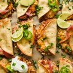 baked crispy pork tacos topped with herbs, lime wedges, avocado and sour cream.