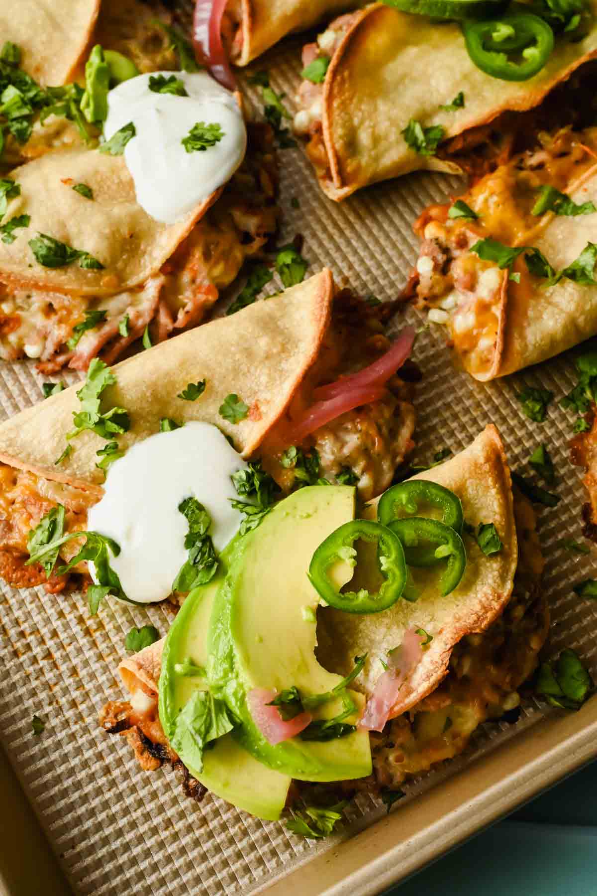 baked crispy pork tacos topped with herbs, lime wedges, avocado and sour cream.