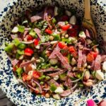 dense bean salad with chopped tomatoes, mozzarella, and salami pieces in large speckled bowl.