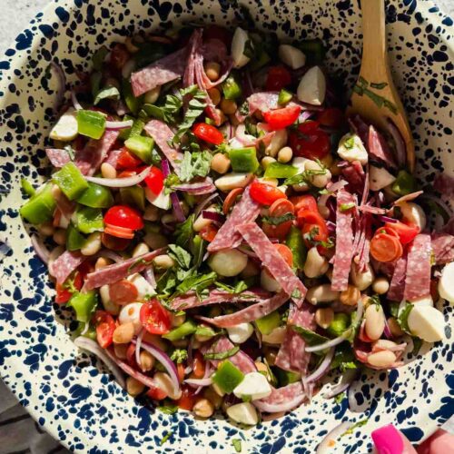 dense bean salad with chopped tomatoes, mozzarella, and salami pieces in large speckled bowl.