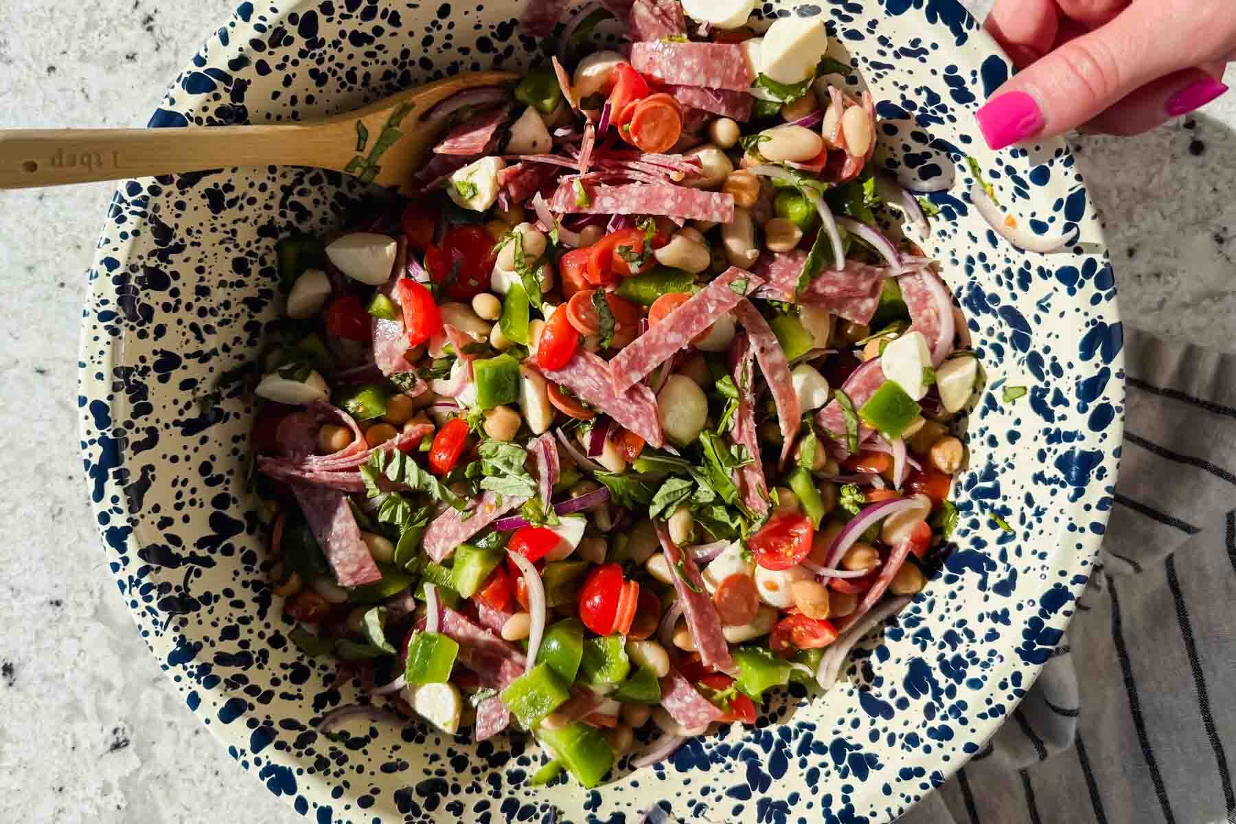 dense bean salad with chopped tomatoes, mozzarella, and salami pieces in large speckled bowl.
