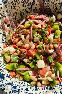 dense bean salad with chopped tomatoes, mozzarella, and salami pieces in large speckled bowl.