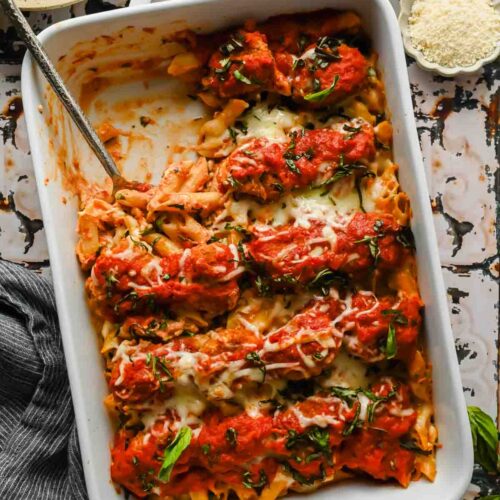 baked healthier chicken parm in rectangular baking dish topped with melted mozzarella and spoon taking out a serving.