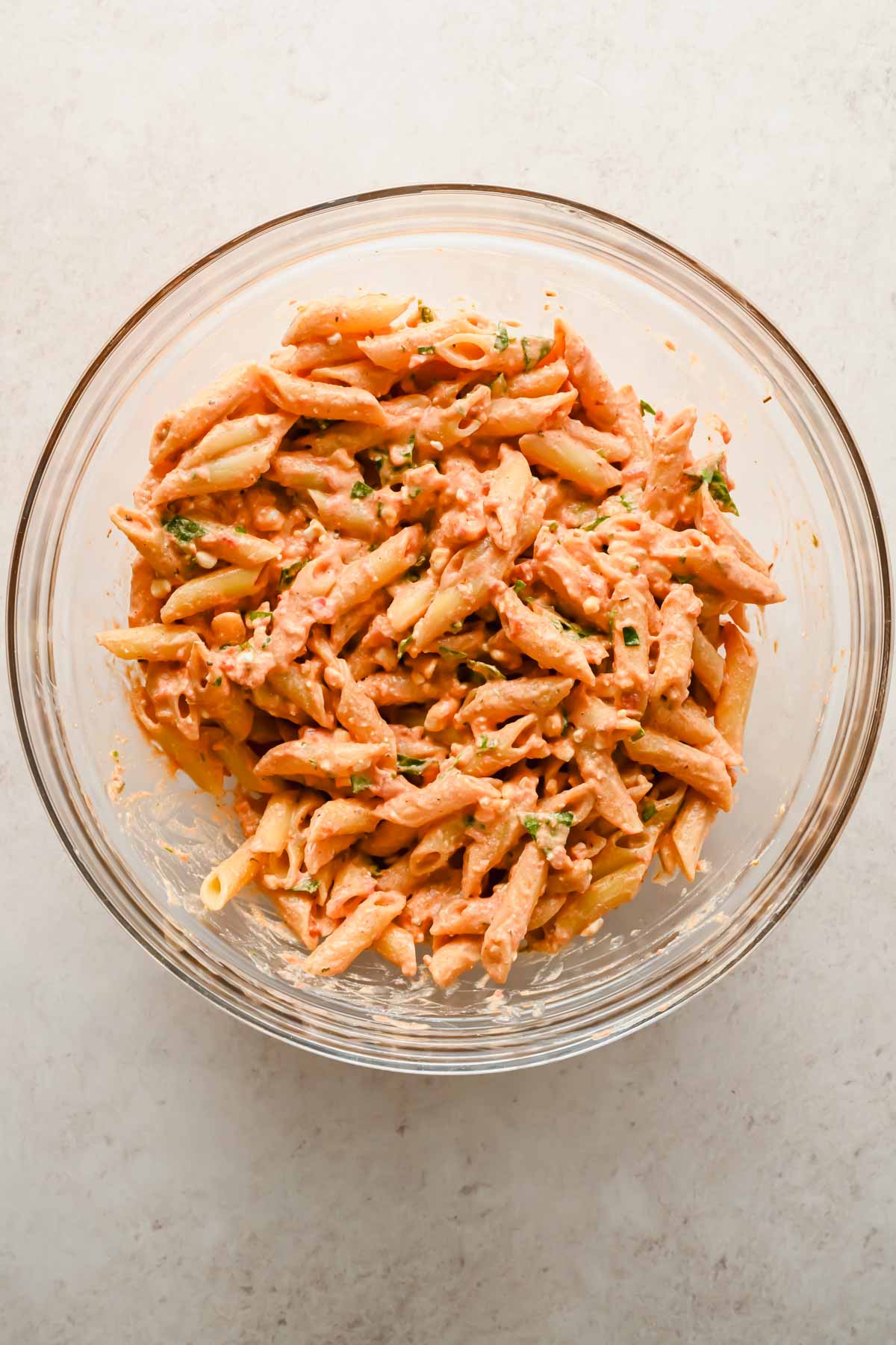 penne noodles mixed with creamy tomato sauce in glass mixing bowl.